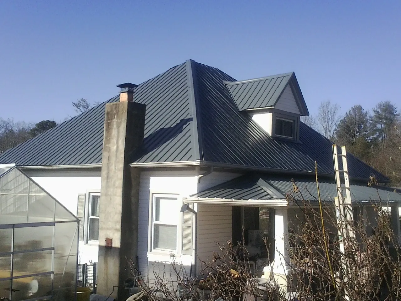 Dark blue standing seam metal roof on a white farmhouse with dormer — Slate & Tile Roof Repair by Roofing Brothers in Roundup