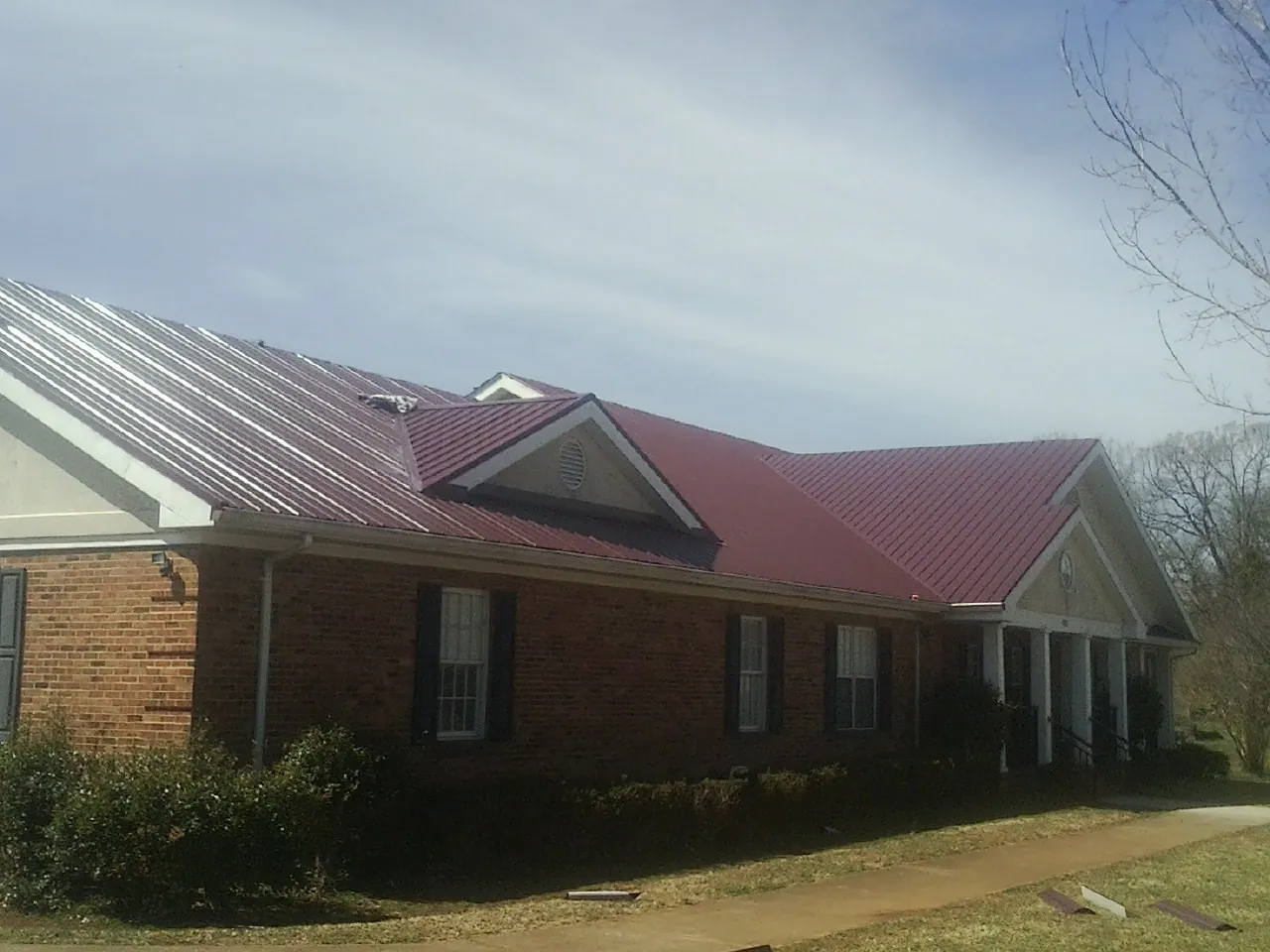 Red metal roof with gabled entries on a long brick building, from a Hail Damage Roof Repair job in Roundup
