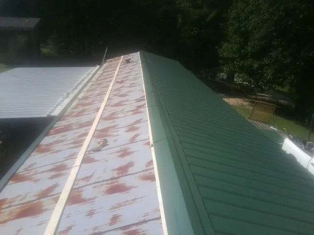 Old rusted panels beside newly installed green metal roofing — Wind Damage Roof Repair by Roofing Brothers in Roundup