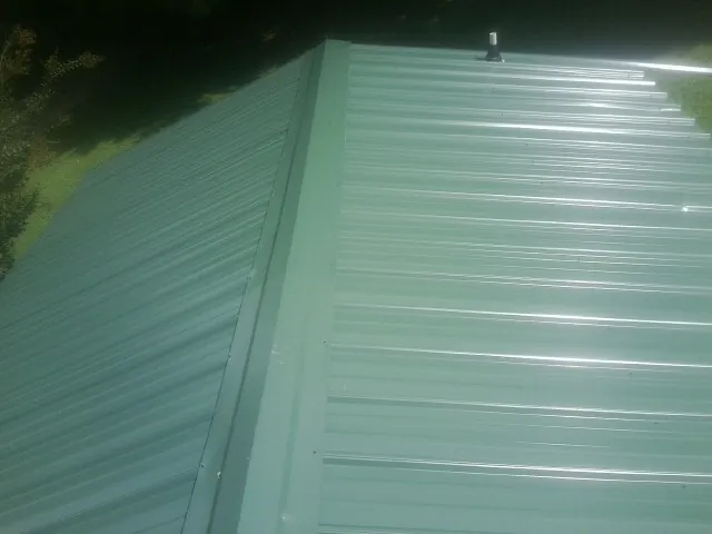 New green metal panels meeting at the ridge of a roof — Flat Roof Repair work by our crew in Roundup