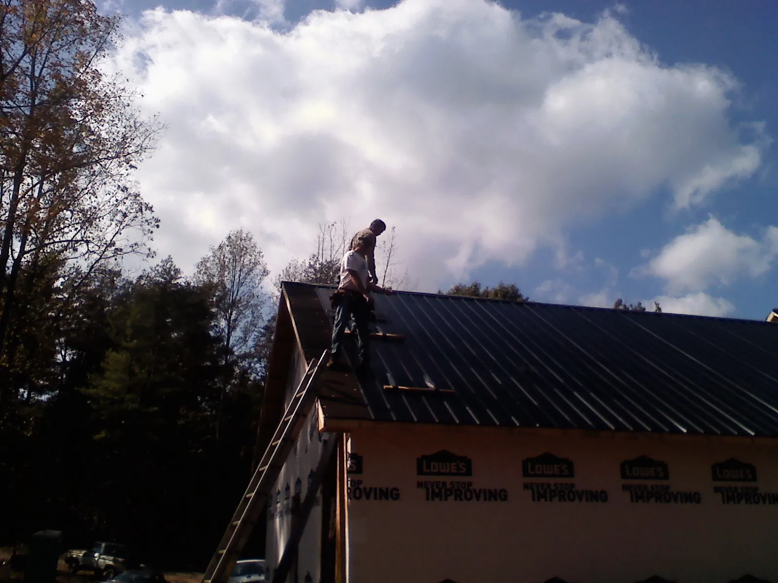 Roofer fastening dark metal panels high against a cloudy sky, from a Roof Inspection job in Roundup