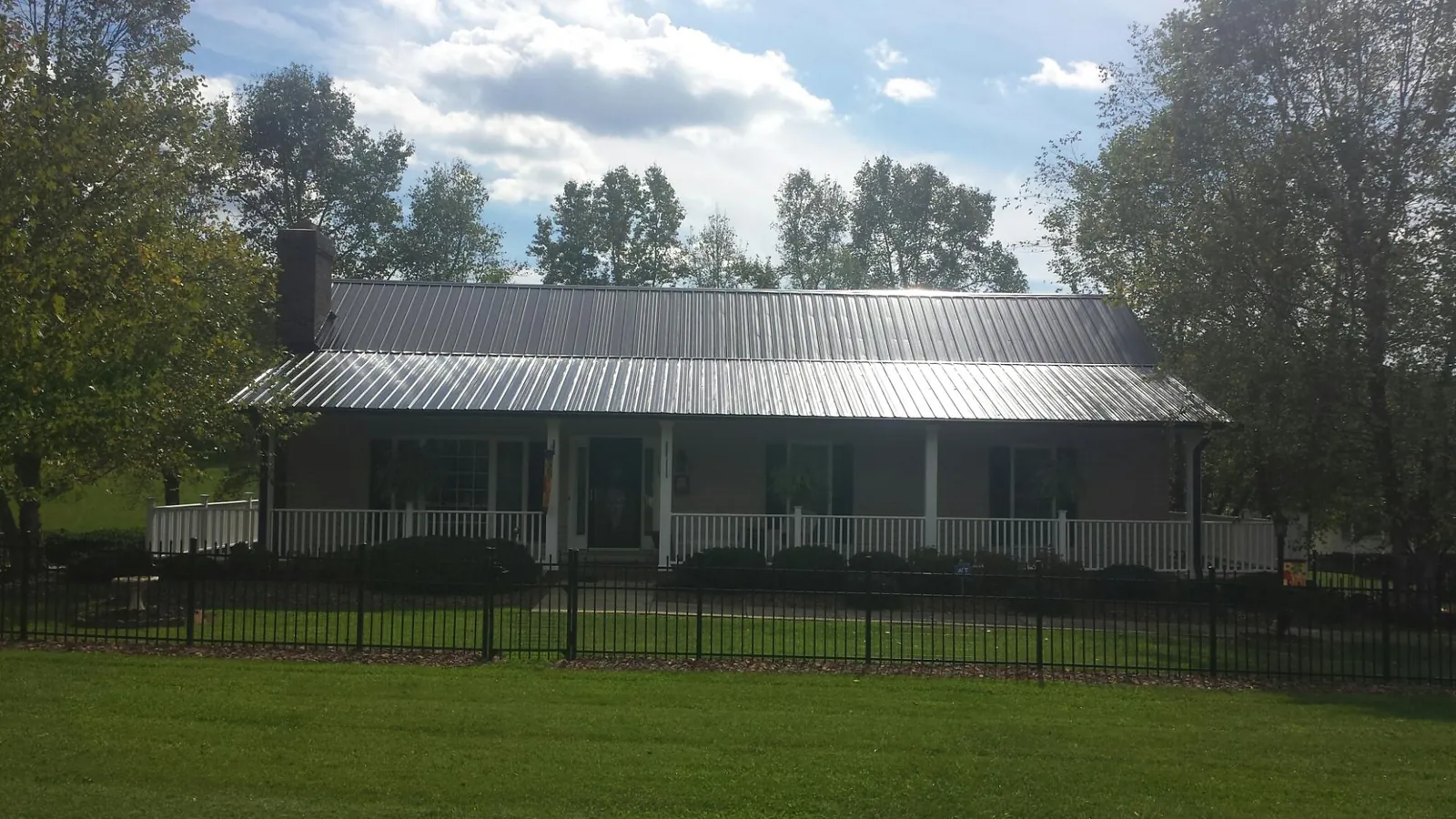 Gray metal roof on a brick ranch with a full width front porch — Gutter Guard Installation work by our crew in Roundup