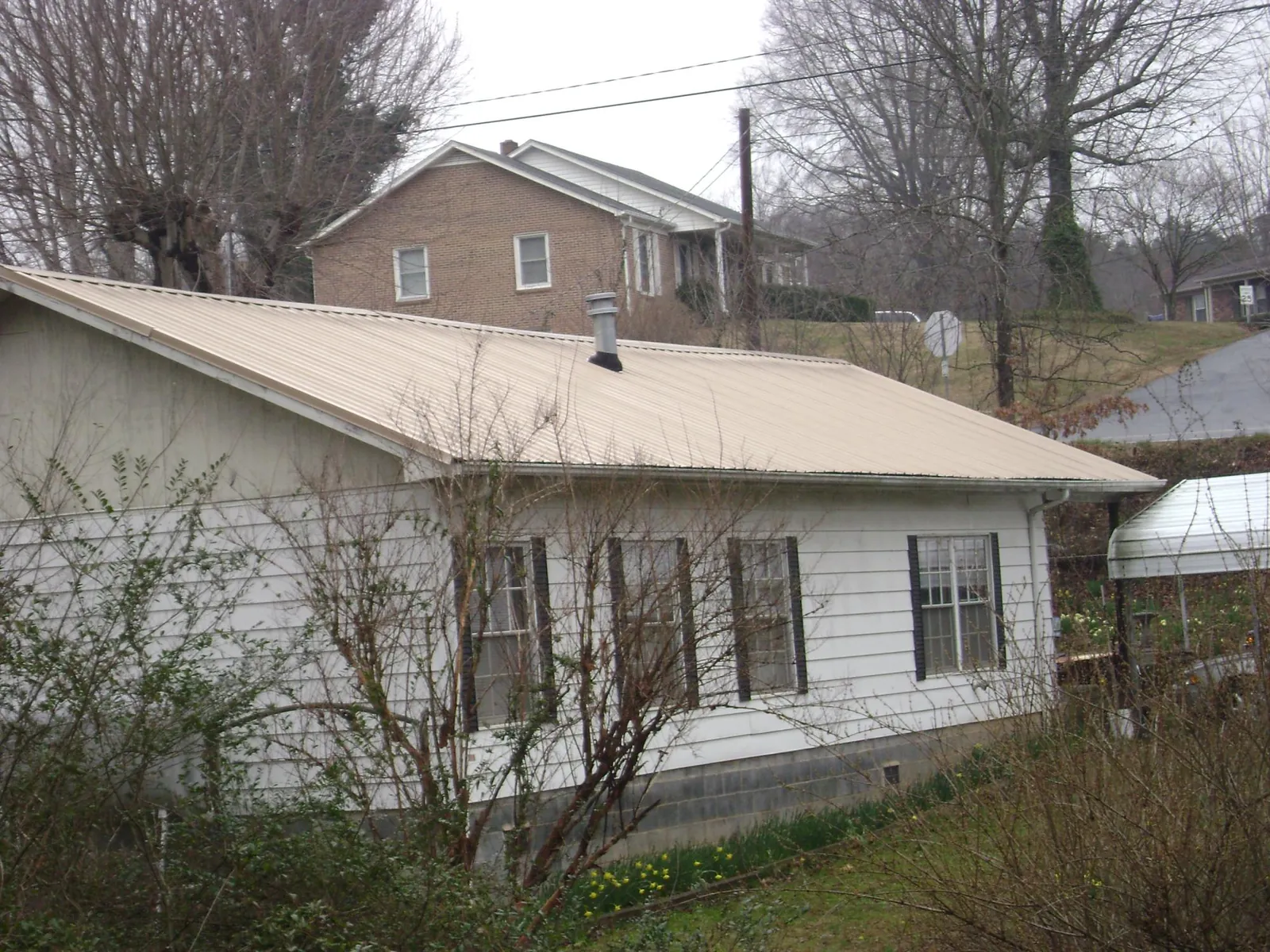 Tan metal roof on a white sided house set into a hillside — Commercial Roofing by Roofing Brothers in Roundup